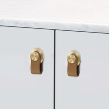 Загрузить изображение в средство просмотра галереи, Leather cabinet knobs with brushed brass and zinc alloy base installed on a white cabinet, European style by Triumph Hardware.