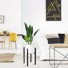 Load image into Gallery viewer, Modern living room with adjustable matte black plant stand, holding a vibrant green plant beside a white sofa and geometric wall art.