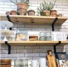 Load image into Gallery viewer, Wooden shelves with black iron brackets holding pottery, glassware, and cookbooks against a tiled wall.