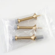 Triumph Hardware hinge pin door stoppers are displayed in a product collage.  Available finishes include matte black, gold, satin nickel, and polished chrome. Features include solid metal construction, adjustable angle with rubber bumpers to prevent wall damage, and a diagram illustrating easy installation on a standard door hinge.  Applicable for bedroom, bathroom, and study doors for mute, protective use.