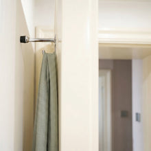 Load image into Gallery viewer, Wall-mounted zinc alloy door stopper hook installed behind a door, holding a hanging garment.
